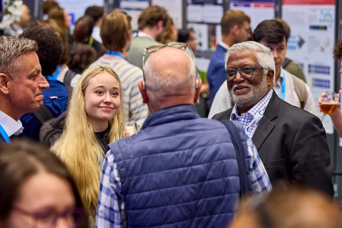 Smiling conference attendees enjoy a chat in an exhibition hall during a scientific poster session.