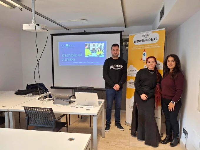 Tres personas posan en un aula junto a una pantalla de proyección en la que se muestra una presentación titulada “Cambia el rumbo”. En la mesa hay un ordenador portátil y material de trabajo. A la derecha se ve un roll-up de Ingeus con el título “Bienvenidos/as” y gráficos explicativos del proceso de acompañamiento al empleo.