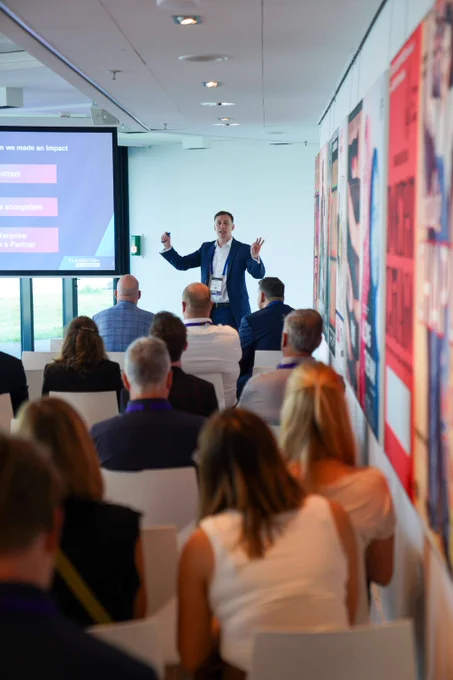 Business professional giving a presentation to an attentive audience in a modern conference room with colorful wall art.