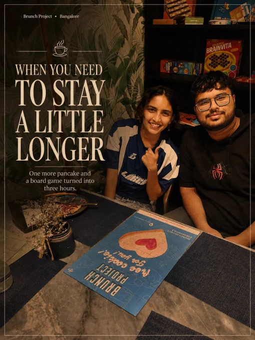 Aesthetic brunch café interiors and lifestyle moments at The Brunch Project in Koramangala, Bangalore. The collage-style visuals showcase cozy marble-top café seating with woven blue chairs, warm natural sunlight, hanging plants, and elegant neutral-toned interiors designed for relaxed brunch experiences. One image features a specialty coffee cup with soft latte art beside dried flowers and typography reading “When you need to catch up.” Another shows guests enjoying a board game and brunch session with the line “When you need to stay a little longer,” highlighting the café’s warm social atmosphere. The final visual displays a full brunch spread with pancakes, burgers, milkshakes, eggs, coffee, and comfort food plates styled on a marble table surrounded by lush greenery. The mood is cinematic, cozy, and inviting, reflecting Bangalore’s modern café culture and the experience of slow mornings, meaningful conversations, specialty coffee, and long brunch catch-ups at The Brunch Project.