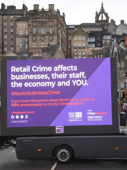 A digital billboard on a truck displays a message about retail crime, with the hashtag #NotAVictimlessCrime.