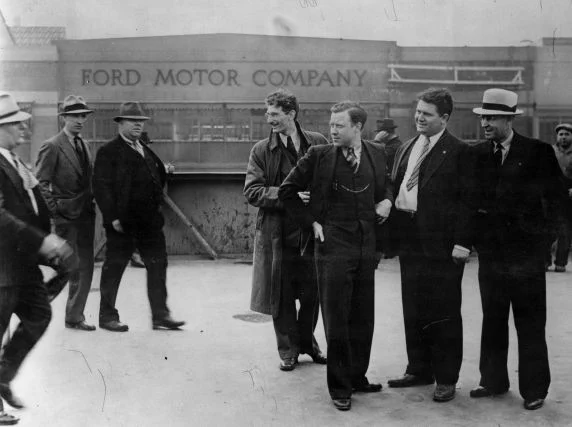 UAW organizers pose for the press on the Miller Road Overpass as members of the Ford Service Department approach. Moments after this image was taken the organizers were savagely beaten by the servicemen in the incident that would become known as the Battle of the Overpass.

Left to right: Robert Kanter, Walter P. Reuther, Richard Frankensteen, J.J. Kennedy