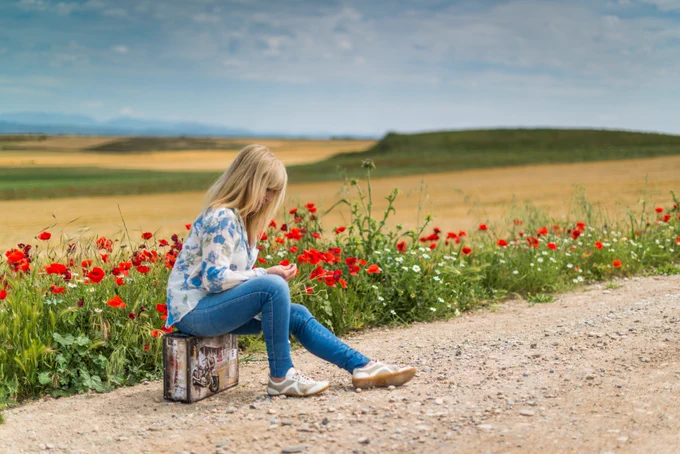 Young woman sitting by the edge of a field, with face obscured by her hair and poppies behind her