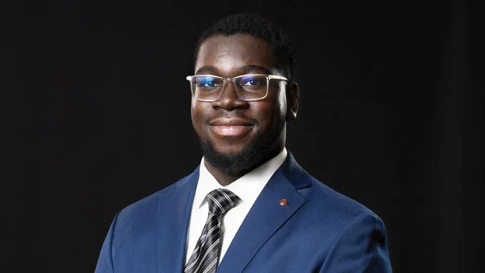 Pictured is Luke Andy Boateng on a dark background. He is in a blue suit with a white collar shirt.