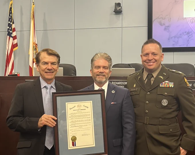 Three men stand together holding a framed resolution recognizing Florida Tech’s commitment to veterans and military families. The group poses smiling during the Brevard County Commission presentation honoring Florida Tech’s seventh consecutive year as a Military Friendly School.