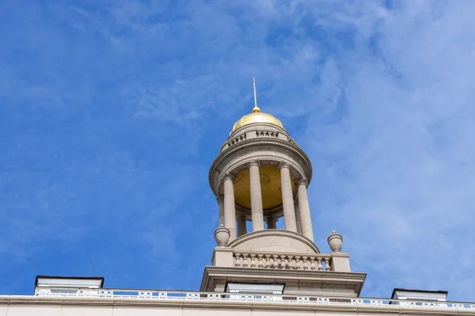 The image shows the top section of a historic SMU building featuring a distinctive golden dome and classical architectural details set against a clear blue sky.