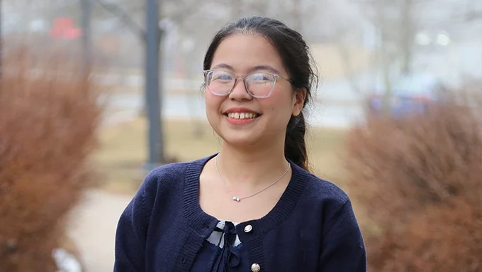 Tam Nguyen is smiling at the camera with an early spring scene behind her.