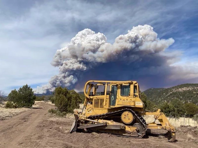 Dozer with wildfire smoke in background. Dozers can construct several miles of containment line in a day and are  essential to maintaining roads and opening up roads for other incident management personnel, hand crews and engines. (Forest Service photo by Dan Quinn)  