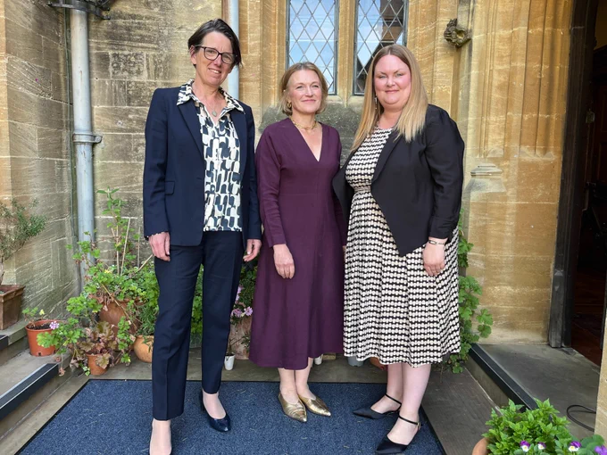 A colour photograph of three women standing in the entrance to an old stone building at Mansfield College in Oxford. From left to right: Anne Keast-Butler (Director of GCHQ), Helen Mountfield KC (Principal of Mansfield College), and Dr Claire Hubbard-Hall (speaker at the event).