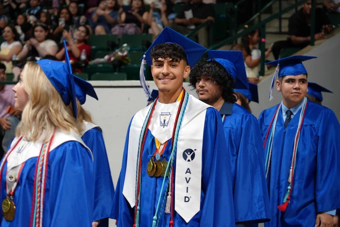 A group of graduates wearing blue caps and gowns, with one holding a medal, posing for a photo.