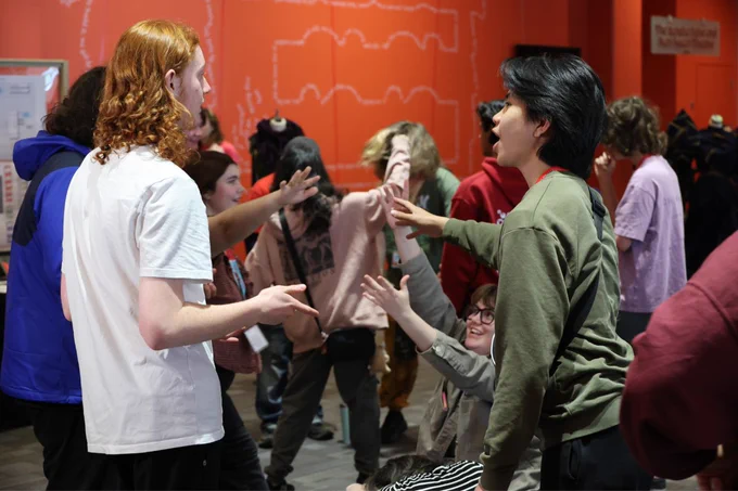 A group of people engaged in animated conversations inside a room with bright orange walls.