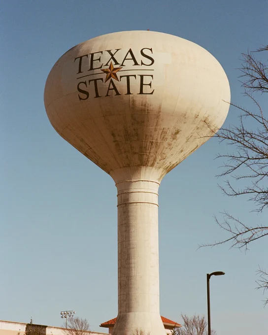 Tall water tower with Texas State logo and star against a clear blue sky.