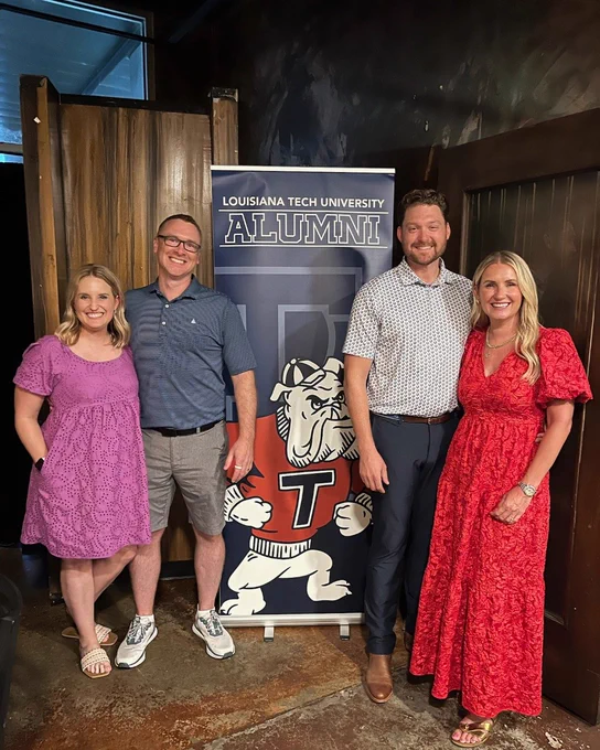 Four people stand on the side of a Louisiana Tech alumni vertical banner