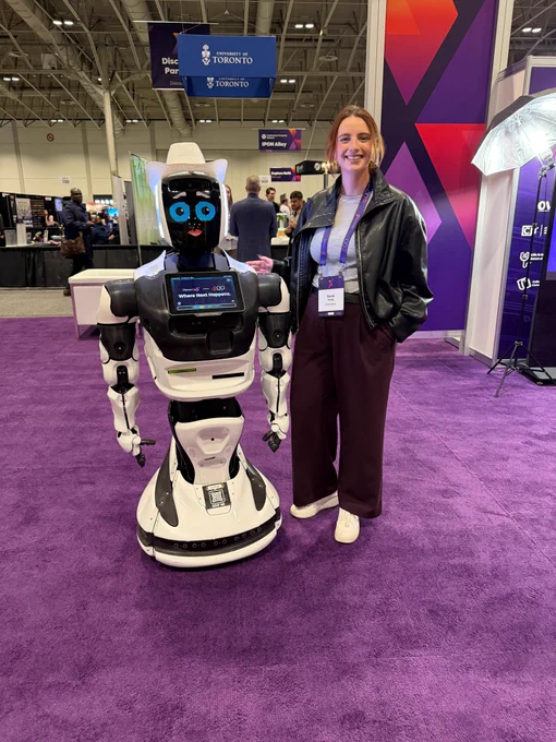 Person standing next to a robot wearing a hat. 