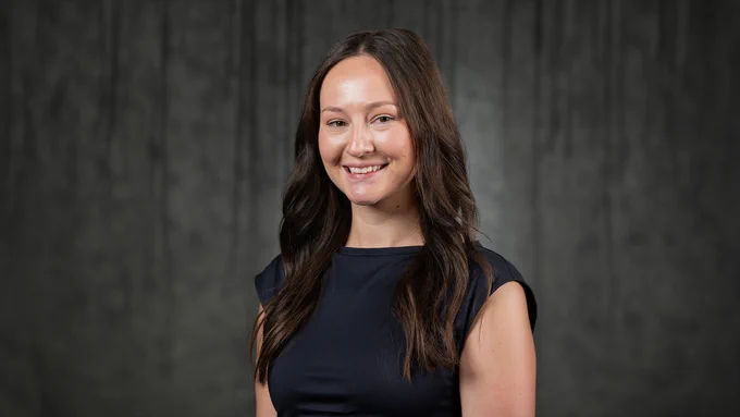 A woman wearing a black top smiling in front of a grey backdrop.