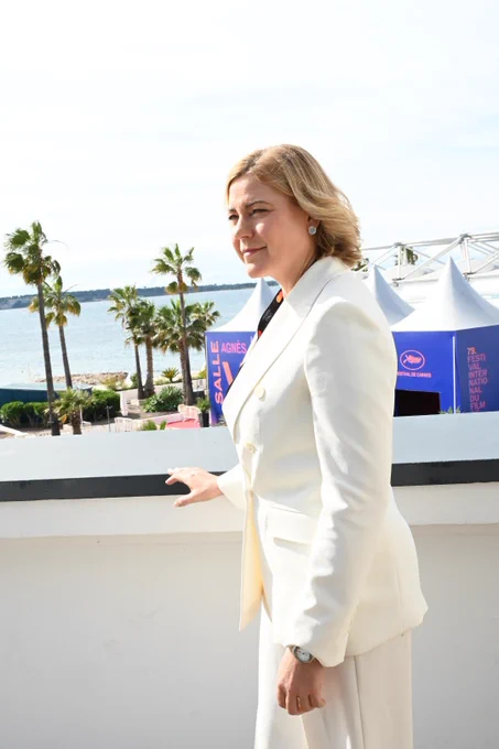EVP Henna Virkkunen stands on a terrace overlooking the waterfront and palm trees near the Cannes Film Festival venue, wearing a white suit in bright daylight.