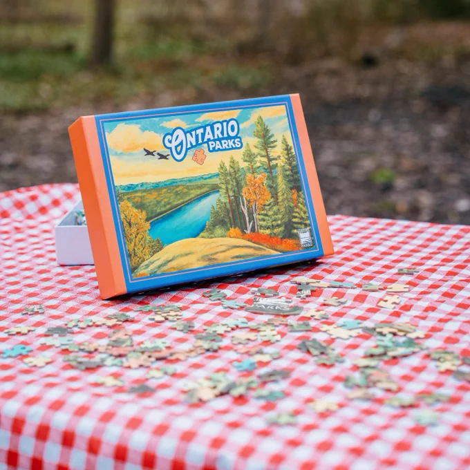 Ontario Parks puzzle showing a illustration of a high rocky outcrop and fall forest overlooking a river, birds and Ontario Parks title in the sky.