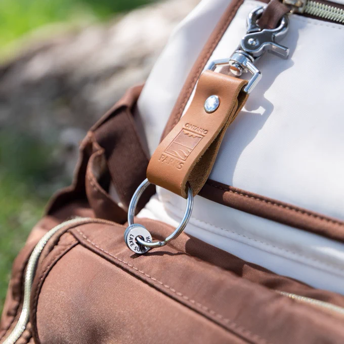 Closeup of the Ontario Parks Traveller Collective Clip. This leather keychain has the Ontario Parks logo embossed on it and traveller collectable rings with park names on the keychain loop. 