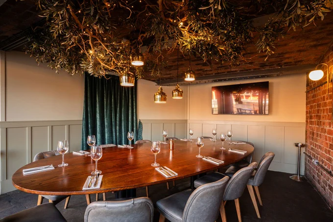 Privatw dining room with a large oval wooden table set with wine glasses and cutlery, surrounded by upholstered chairs, under warm pendant lights.