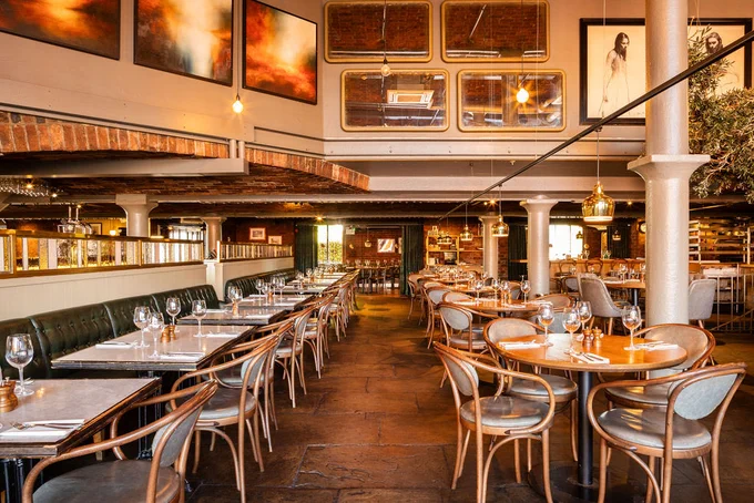 Stylish open-plan restaurant with brick features, marble and wooden tables, curved wooden chairs, soft ambient lighting and a mix of booth and table seating.