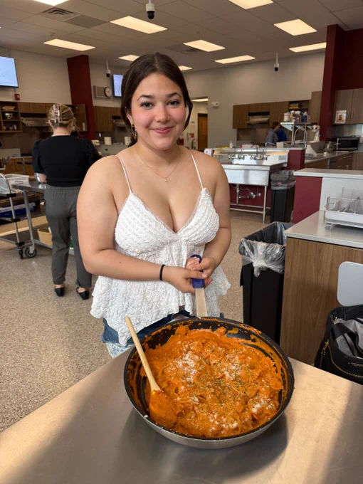 A woman in a white tank top holding a large casserole dish filled with what appears to be a baked pasta dish or casserole.