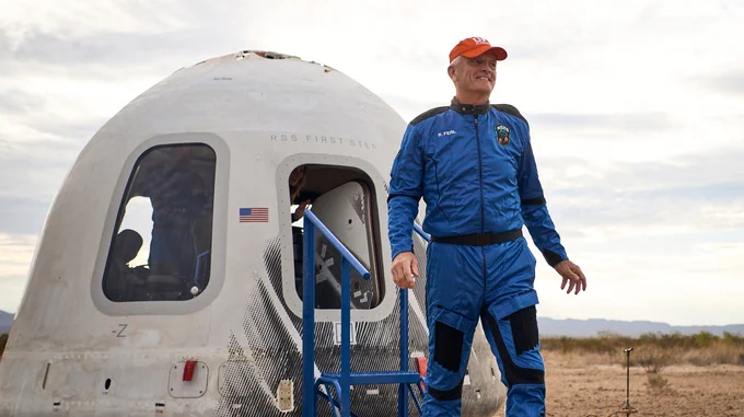 Doctor Rob Ferl smiling while stepping off of a space craft, wearing a Blue Origin space suit and U F baseball cap.