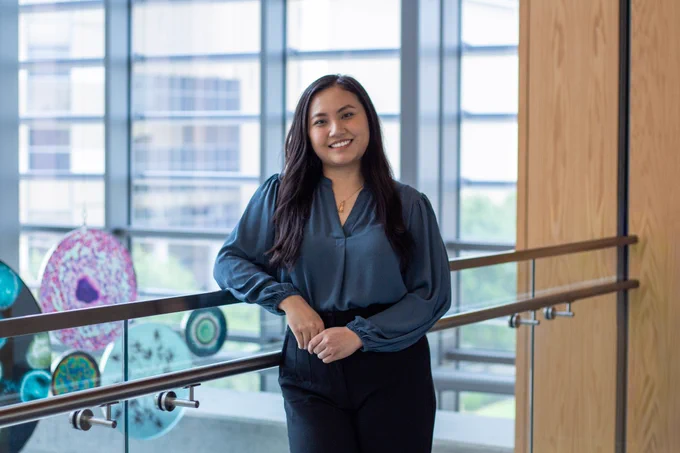 Anh smiles for a portrait inside the Health Education Center, standing near a railing with large windows in the background.