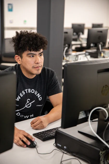 Alt text: A student sits at a desktop computer in a computer lab.