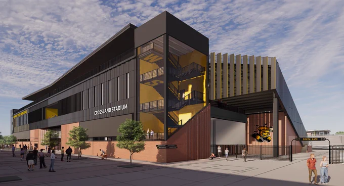 A modern sports stadium named Crossland Stadium with a sleek design featuring large glass sections and bold black and brick accents. The structure includes visible staircases and Wichita State University branding. Several people are walking near the entrance under a clear blue sky.