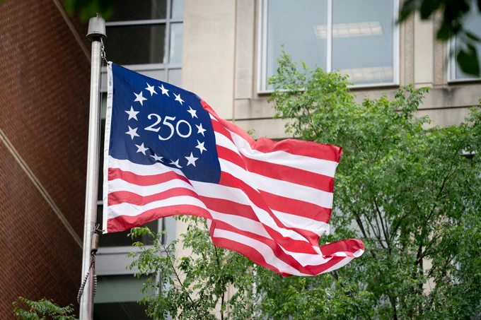 Image of the America 250 Flag blowing in the wind after being raised. 