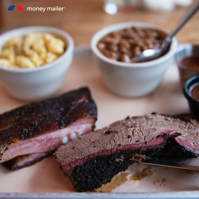 Close-up of sliced smoked brisket and ribs with bowls of baked beans and macaroni and cheese in the background.