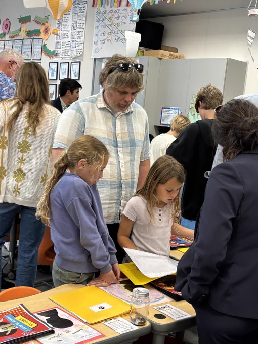 Two students and an adult review classroom work and folders during an elementary school family event.