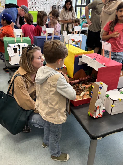 Families and students gather around colorful student-made projects during a busy elementary classroom open house.