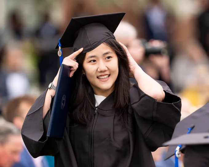 A graduate in robes adjusting their hat