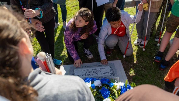 Oklahoma School for the Blind students surrounding headstone dedicated to Lura A. Lowrey.