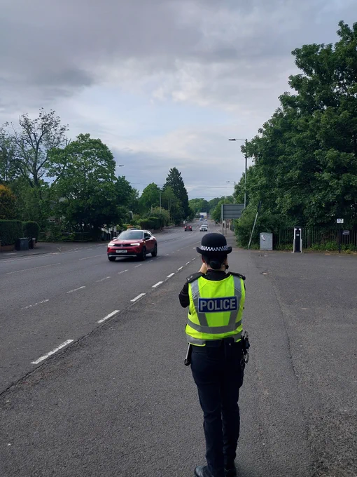A police officer in uniform conducting speed checks on a road with cars and trees.