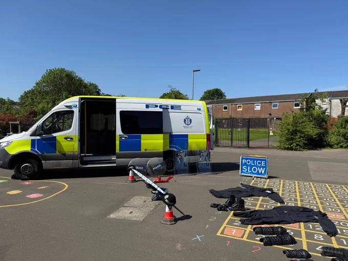 Police van and public order gear laid out on a playground with a 'POLICE SLOW' sign.