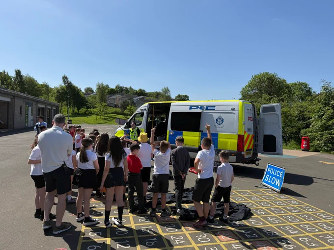 Children gathered around a police van in a schoolyard with a police officer.