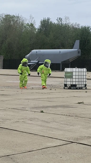 two people in hazmat suits in front of a fake airplane