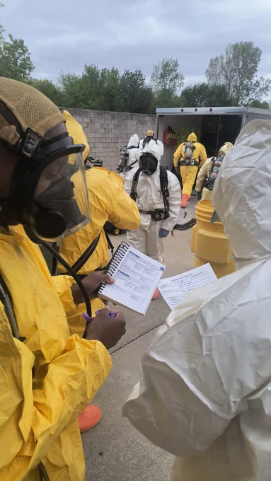 people in hazmat suits reading from a book