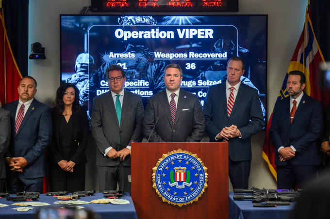 Group of six officials standing behind a podium with FBI seal during Operation VIPER press conference displaying arrests and weapons recovered.