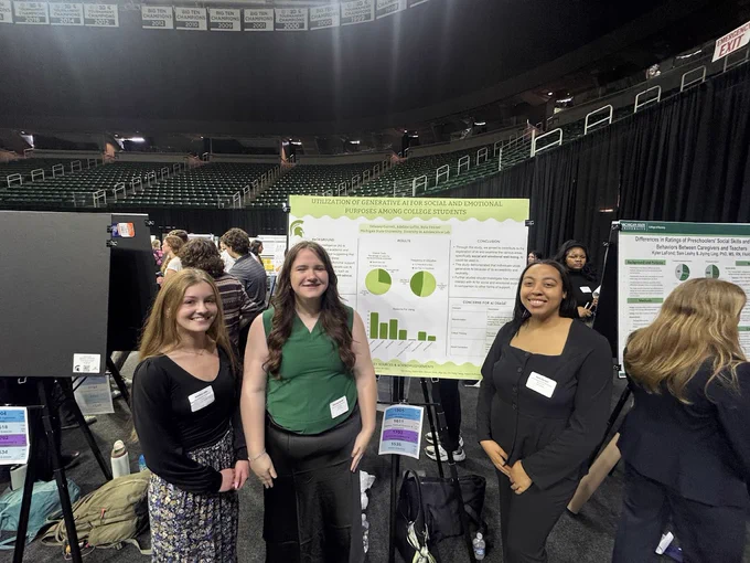 Three smiling young women stand in front of a research poster titled \"UTILIZATION OF GENERATIVE AI FOR SOCIAL AND EMOTIONAL PURPOSES AMONG COLLEGE STUDENTS\". Other researchers and posters are visible.