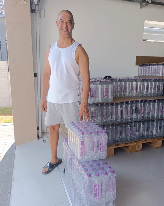 A picture of Moses, from Fairview in Port Elizabeth standing next to cases of Designer Water pH10.