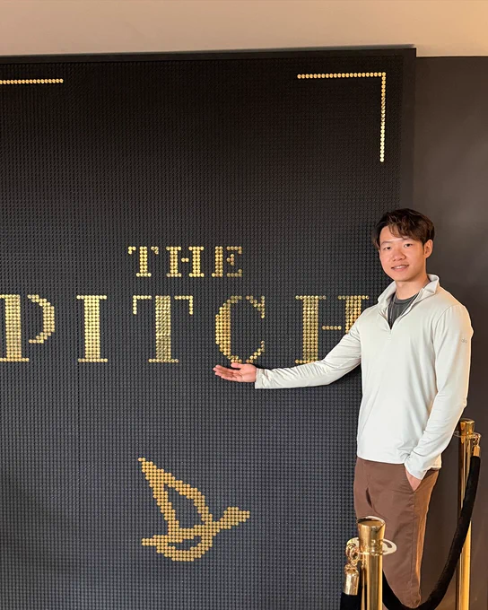 Daniel gestures toward a black wall with the words "THE PITCH" in gold lettering.