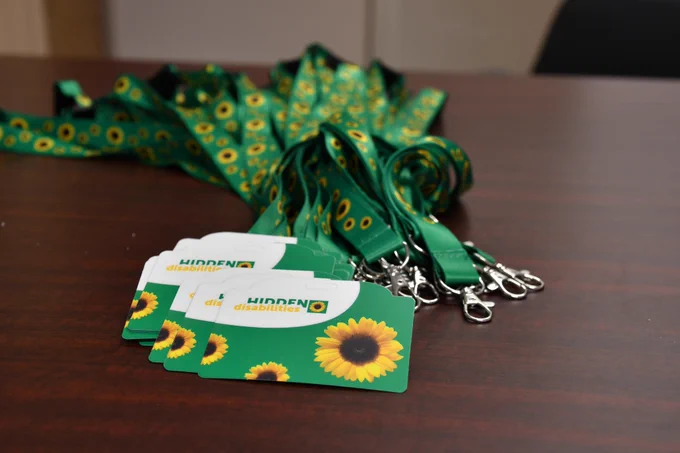 Image of a stack of Sunflower Lanyards. Credit-card sized cards say Hidden Disabilities on them, with images of Sunflowers. The lanyards are green with sunflowers printed on them. 