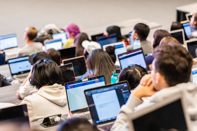 Students seated in a lecture hall, focused on their laptops during a class session.