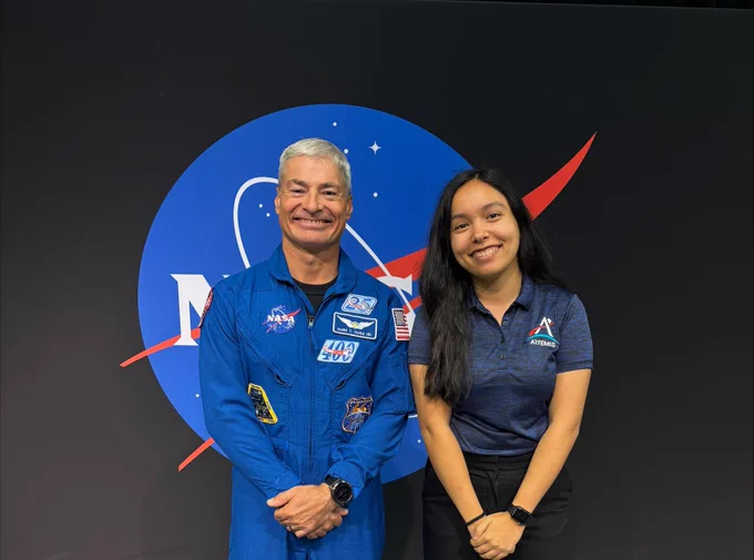 Hannah with Astronaut Mark Vande Hei posing for a photo in front of a wall with the NASA logo on it