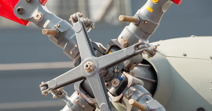 Close-up view of a helicopter rotor hub with red components, showcasing mechanical details and bolts.