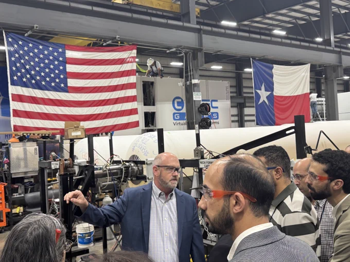 Delegates participate in site tour of Hydria Gas Technologies manufacturing plant. Images of U.S. and Texas flags in background.

