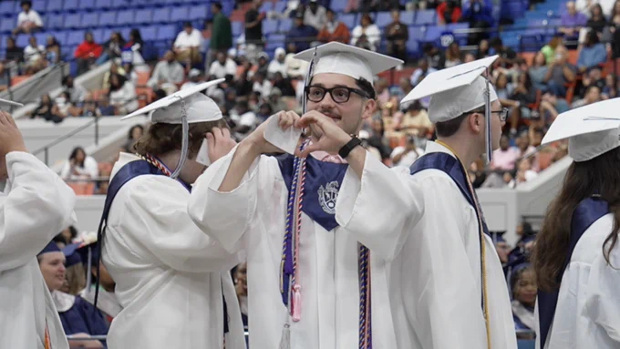 A graduate makes a heart sign with his hands.